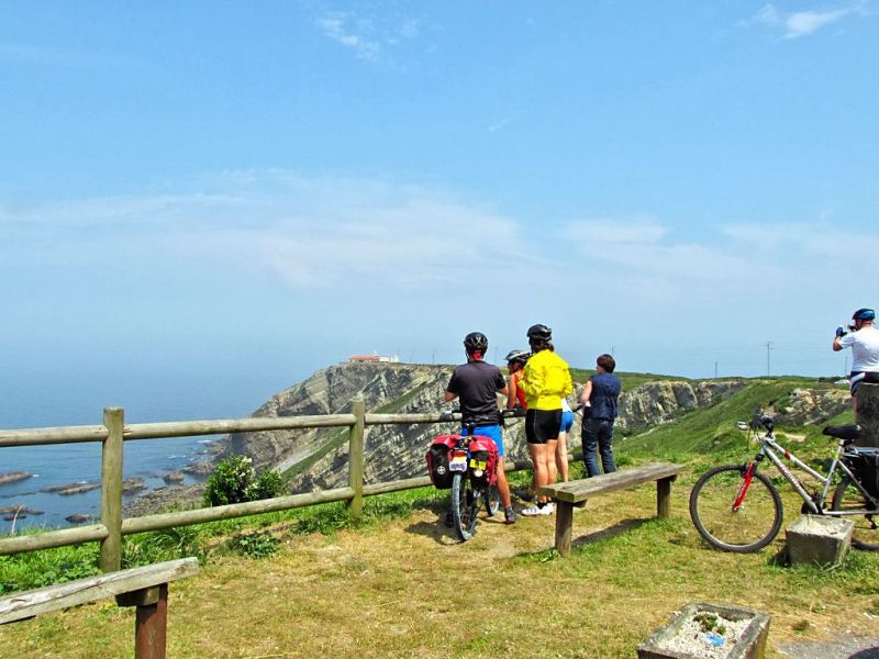 Cicloturistas en Oviñana cerca del Faro Vidio (al fondo)